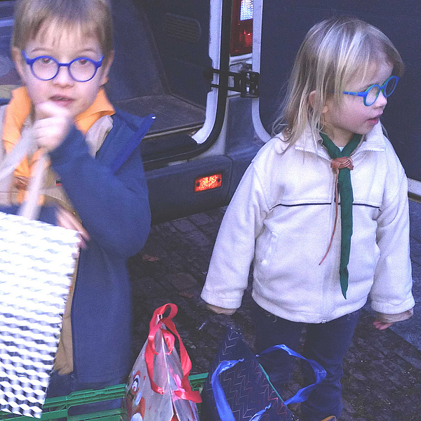 Ein Junge und ein Mädchen in Pfadfinderkleidung laden Geschenke aus einem Fahrzeug aus,
